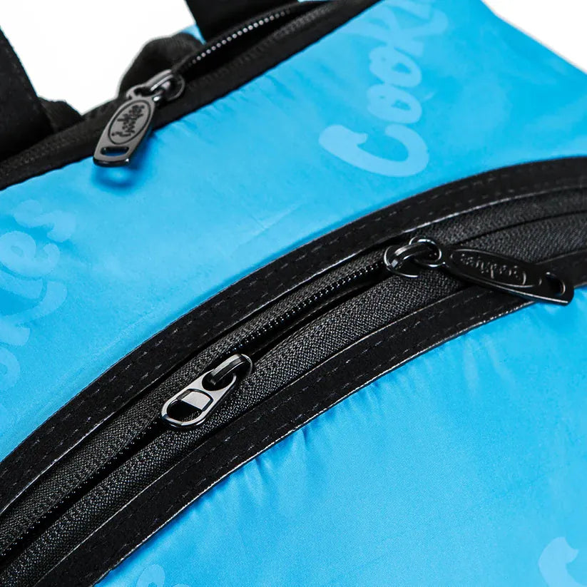 Bright blue satin backpack with all-over subtle "Cookies" logo pattern and black zippered pockets with metal pulls.