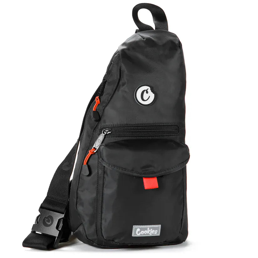 Black nylon traveler sling bag with smell-proof lining, adjustable strap, and multiple pockets. Features orange zipper pulls and a red accent tab.