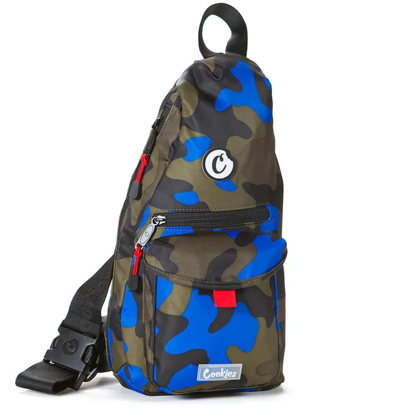 Camouflage print sling bag with blue and green patterns, featuring a main zippered compartment, front pocket with red accent, and 'Cookies' logo patch.