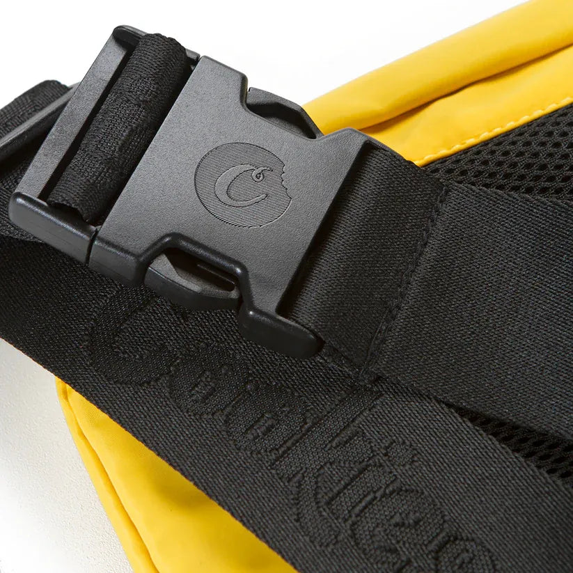 Yellow traveler sling bag with black adjustable strap featuring a black buckle with embossed logo and textured black lettering.